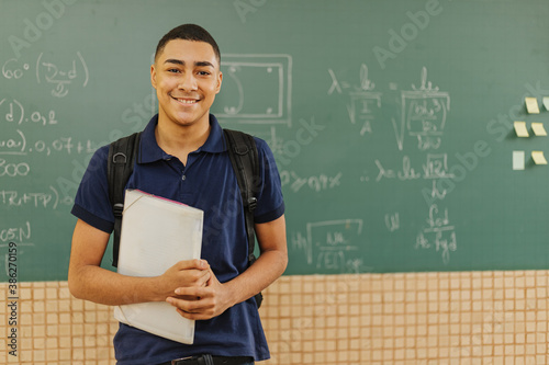 Latin men student smiling wearing backpack holding a notebook in a classroom