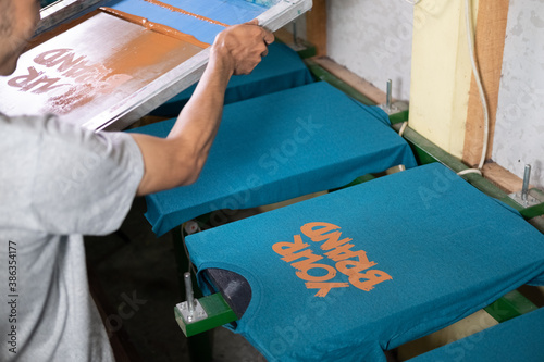 close up of male workers hold and lift the screen printing frames after printing the t-shirts at the workshop