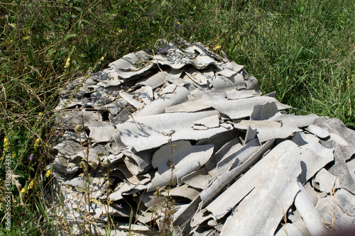 Płytki azbestowe wyrzucone na trawę. Dzikie wysypisko śmieci.