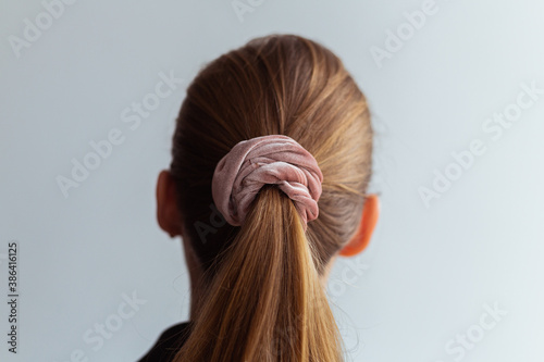 Close-up of a natural blonde hair, tied up in a ponytail by pink velvet scrunchie, back view 