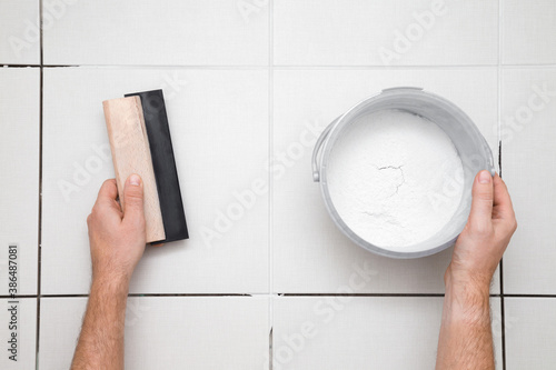 Worker hands holding rubber trowel and powder of grouting paste for ceramic tile seams on floor. Closeup. Point of view shot. Top down view.