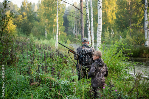 Father's day. Father with gun showing something to son while hunting on a nature. Happy family, Fathers Day and local summer vacation
