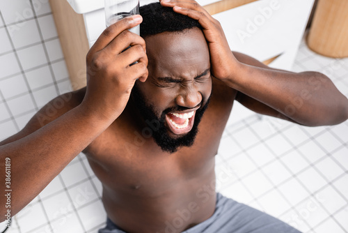 afro-american man screaming from headache and holding glass of water near temple
