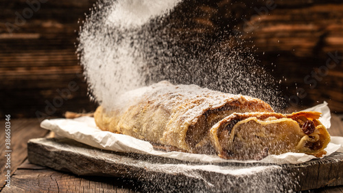 Apple strudel cake with cinnamon and raisins, sieve sprinkling sugar powder from above. austrian germany food