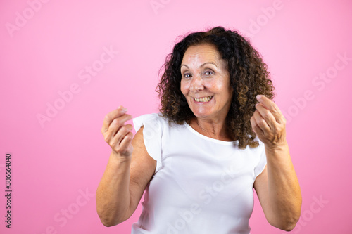 Middle age woman wearing casual white shirt standing over isolated pink background doing money gesture with hands, asking for salary payment, millionaire business