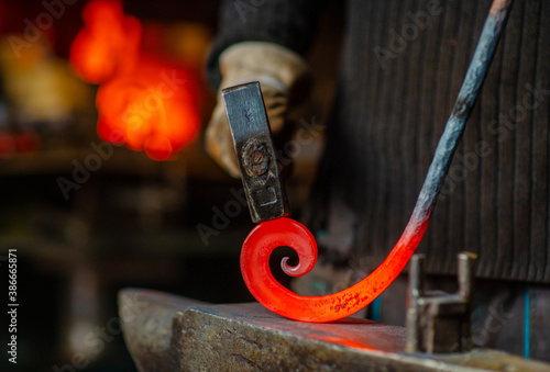 The blacksmith twists the spiral with a sledgehammer, placing a red-hot iron blank on the anvil. Work in the forge