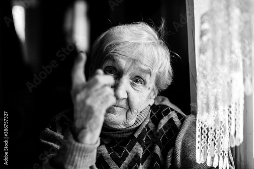 An elderly woman threatens with a finger looking at the camera. Black and white photography.