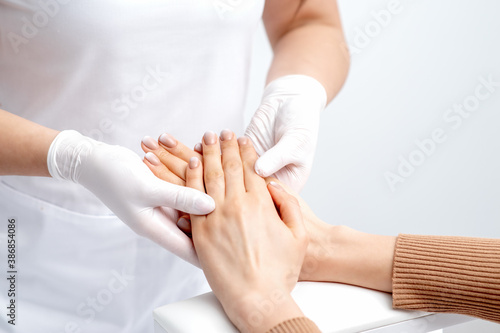 Manicurist wearing gloves doing wax massage on female hands with manicure in nail salon