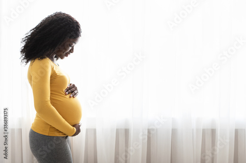 Beautiful pregnant black woman hugging her tummy at home