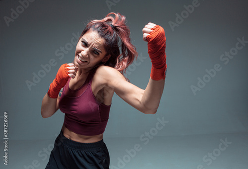 Pretty girl fighter in boxing bandages makes an uppercut in studio isolated on gray background. Strength and motivation