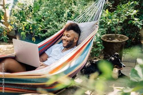 Man relaxing in hammock working on laptop computer 