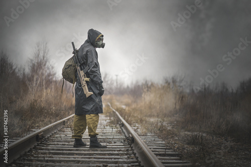 A post apocalypse soldier with a rifle is walking on the railroad.