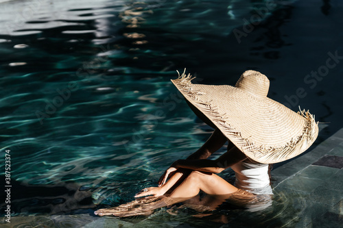 Woman in big straw hat relaxing at pool. Wellness and relaxation concept for summer luxury vacations.