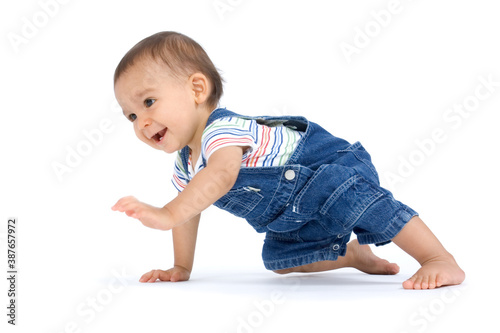 A crawling baby boy dressed in overalls and isolated on white background