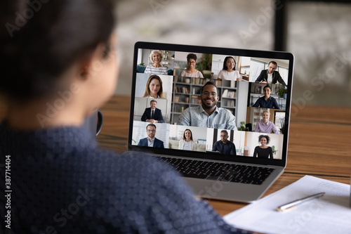 Over shoulder view of female worker have webcam digital virtual conference with diverse multiethnic colleagues. Woman speak talk on video call with multiracial businesspeople. Online meeting concept.