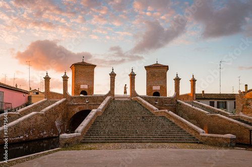 Comacchio, Ferrara / Italy - August 2020: Trepponti Bridge in Comacchio at dawn with a tourist in the center of the columns, sky with clouds