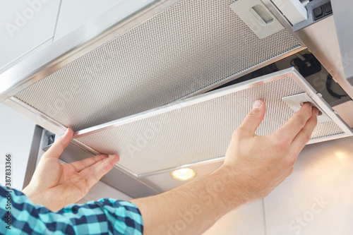 Mans hands removing a filter from cooker hood for cleaning or service. Replacing filter in kitchen hood. Modern kitchen fan or range hood.