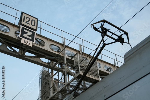 Pantograph of French railways train captating electricty from a catenary overhead line on a railroad infrastructure with train speed signs appearing up of a pole