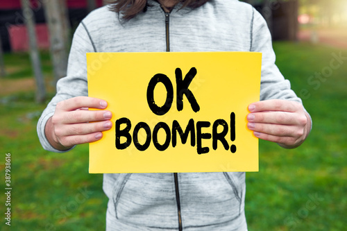 Teenager holds a banner with the word ok boomer against nature background