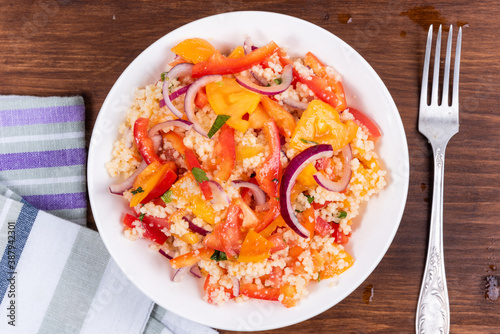 Traditional Mediterranean salad of couscous, tomato, pepper and onion in a plate on a wooden table, close-up, top view - Moroccan and Algerian cuisine