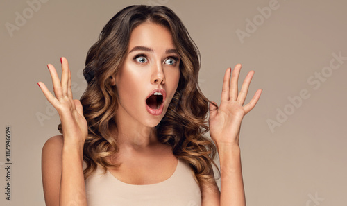 Beautiful shocked and surprised woman screaming and looking to the side presenting your product . Curly hair girl amazed . Expressive facial expressions . Beauty and cosmetology