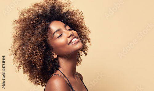 Beauty portrait of african american girl with clean healthy skin on beige background. Smiling dreamy beautiful black woman.Curly hair in afro style 