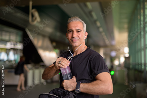 Handsome Persian man with gray hair drinking water at the sky train station