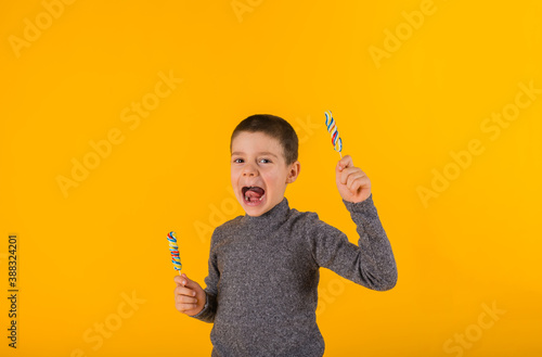 happy little boy with two lollipops on a yellow background with space for text