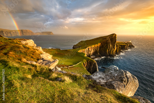 Iconic Isle of Skye lighthouse at Neist Point with beautiful golden light and rainbow over coast. 
