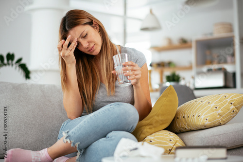 Young woman sick in bed holding glass of water..