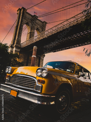 Vintage yellow taxi cab in New York under the Brooklyn Bridge with a colorful sky during sunset