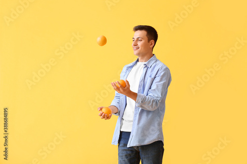 Handsome man juggling ripe oranges on color background