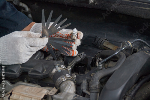 A man with gloves checks the spark plug gap with a feeler gauge