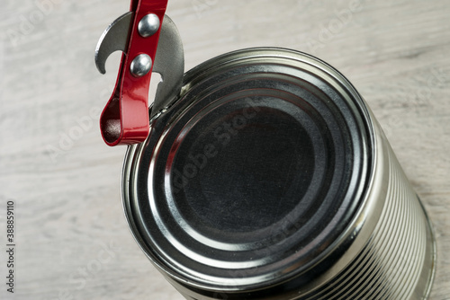 Opening a tin with a can opener..The can opener is on the tin can. Against the background of a blurry table. Selective focus..