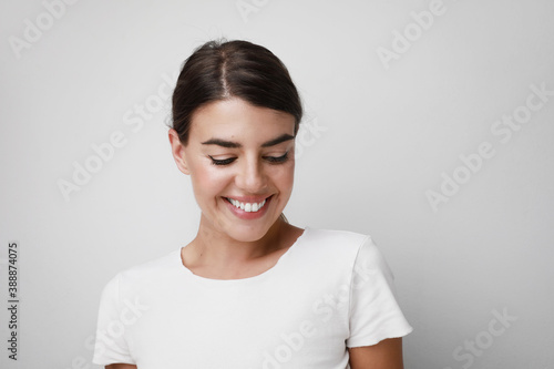 Happy young woman smiling wearing white T-shirt looking down. Space for text.