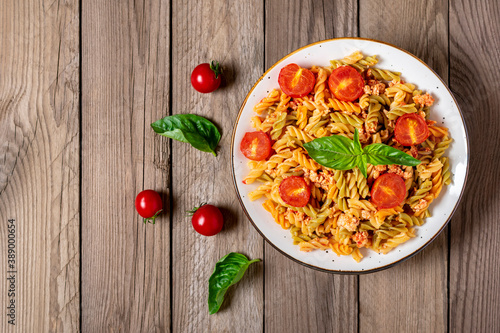 Fusilli - classic italian pasta from durum wheat with chicken meat, tomatoes cherry, basil in tomato sauce in white bowl on wooden table Mediterranean cuisine Top view Flat lay