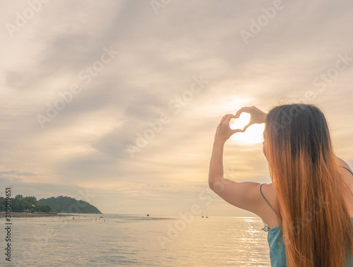 hands making heart shape toward the sky with sunlight, sun reflection on surface of the sea growing like sparkling diamond, golden skycap scenery in summer time, eco tourism love environment concept.