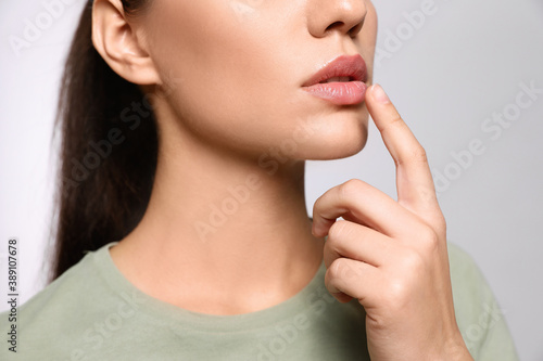 Woman with herpes touching lips on light grey background, closeup