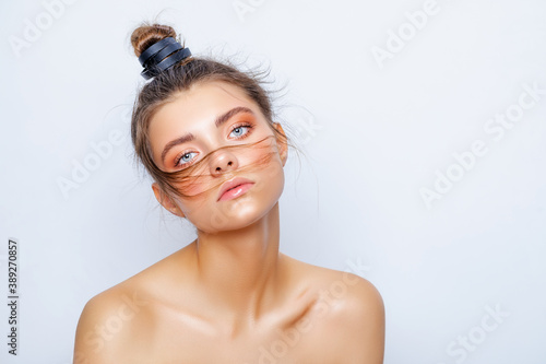Fashion model posing in studio, beautiful girl hair gathered in a bun, glowing make-up. stylish portrait of a fashionable girl, glamorous hairstyle. looking at the camera. 