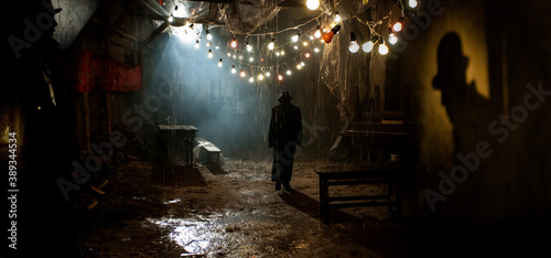 Silhouette of a man in a coat and hat in a dark alley on a rainy night. theme of violence and cruelty