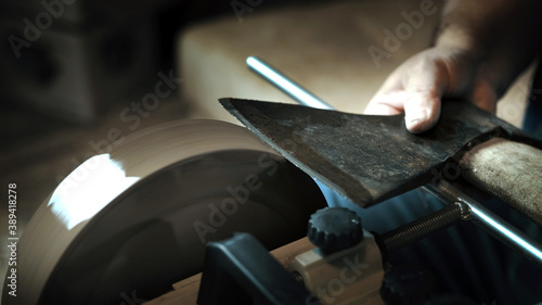 Asian man sharpening axe on a grinder