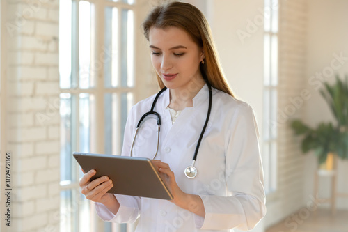 Electronic paperwork. Thoughtful millennial female doctor admitting physician in hospital filling in anamnesis details in medical history files online, making records of patient round results on pad