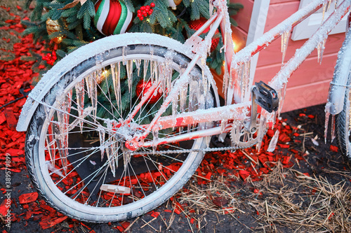 Iced bike with icicles on the background of a Christmas tree near the house, new year