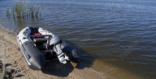 Inflatable boat with outboard motor on the sandy shore by river
