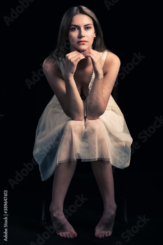 piękna seksowna modelka kobieta dziewczyna w studiu w białej sukience na czarnym tle na krześle