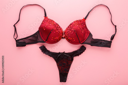 Female black red bra and string panties on light pink table background. Pastel color. Daily underwear. Closeup. Top down view.