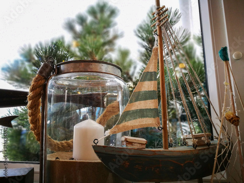 Kompozycja żeglarska, małe drewniane niebieskie żagle i obok kieliszek ze świeczką na tle sosnowych gałązek