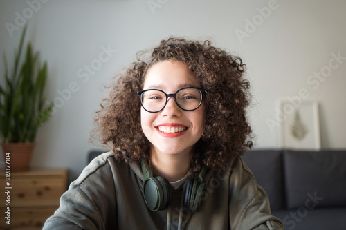 girl looks at camera and smiles. student talks over Internet. Video Conference or e-learning at home. portrait of teen at wide angle.