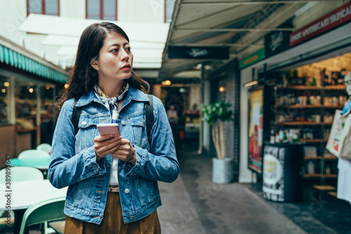 asian woman holding smartphone and looking away is seeking a store. korean lady just moving and living alone overseas is trying to get familiar with the environment.