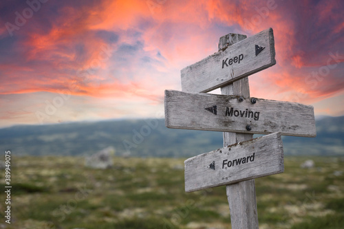 keep moving forward text engraved in wooden signpost outdoors in nature during sunset and pink skies.